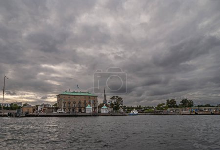 Photo for Copenhagen, Denmark - September 14, 2010: Wide cityscape of harbor west quay with Churchillparken at center. Frederiks Church dome peeks over white fountain. Gray cloudscape - Royalty Free Image