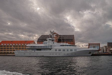 Téléchargez les photos : Copenhague, Danemark - 14 septembre 2010 : Vue depuis l'eau du port, le Mega Super Yacht SKAT amarré dans le port a une couleur et un design militaires sous un paysage nuageux gris foncé. Toits à l'arrière - en image libre de droit