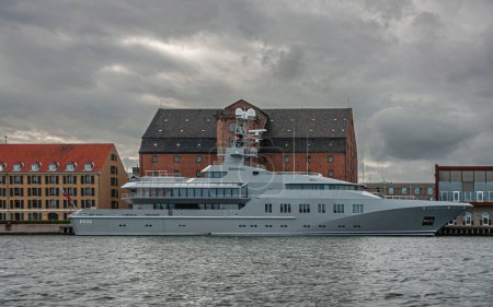 Téléchargez les photos : Copenhague, Danemark - 14 septembre 2010 : Vu de l'eau du port, le SKAT Mega Super Yacht amarré au port a une couleur et un design militaires sous un paysage nuageux gris foncé. Bâtiments à l'arrière - en image libre de droit