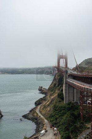 Photo for San Francisco, CA, USA - July 12, 2023: Golden Gate Bridge north side half hidden by thick fog. At bottom, small road leading to historic Lime Point lighthouse. Wider bay water - Royalty Free Image
