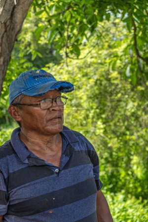 Téléchargez les photos : Zihuatanejo, Mexique - 18 juillet 2023 : Four historique en terre cuite. Portrait du propriétaire, vêtu de bleu, et exploitant du four produisant des briques et des panneaux de toit. Feuillage vert comme toile de fond - en image libre de droit