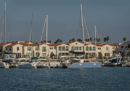 Photo for Ventura, CA, USA - September 14, 2023: Boaters Lounge building with beige facade and red roof facing harbor where multiple yachts, sail and motor, are anchored. Line of palm trees. - Royalty Free Image