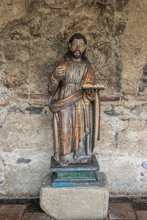 Photo for Guatemala, La Antigua - July 20, 2023: Museum Casa Santa Domingo. San Pablo, Saint Paul wooden sculpture statue on pedestal against gray-brown ruined wall, He holds book in left hand - Royalty Free Image