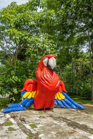 Photo for Costa Rica, Parque Nacional Carara - July 22, 2023: At entrance, giant bright colored statue of Scarlet Macaw. Green foliage backdrop - Royalty Free Image