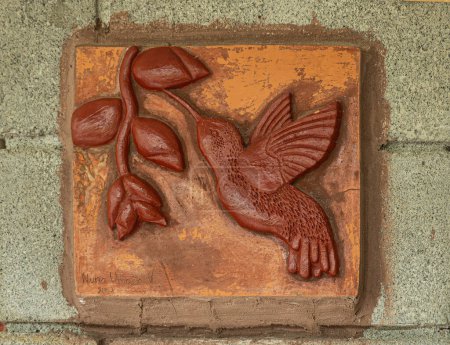Photo for Costa Rica, Parque Nacional Carara - July 22, 2023: Closeup of small red-brown mural by Nuna Umano picturing feeding colibri, hummingbird, set in gray wall - Royalty Free Image