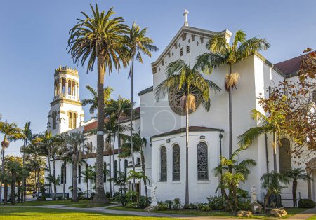 Foto de Santa Barbara, CA, EE.UU. - 19 de enero de 2024: Fachada beige oeste de la iglesia Nuestra Señora de los Dolores con luz solar en la torre contra el cielo azul. Follaje de palmera verde y césped en frente. - Imagen libre de derechos