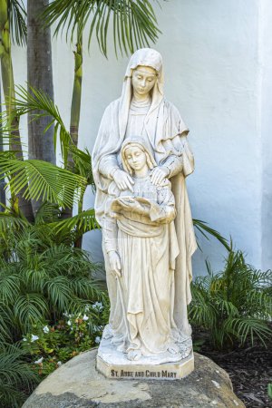 Foto de Santa Barbara, CA, Estados Unidos - 19 de enero de 2024: Primer plano de Santa Ana y su hija María estatua blanca en la roca fuera de la iglesia Nuestra Señora de los Dolores rodeada de follaje verde - Imagen libre de derechos