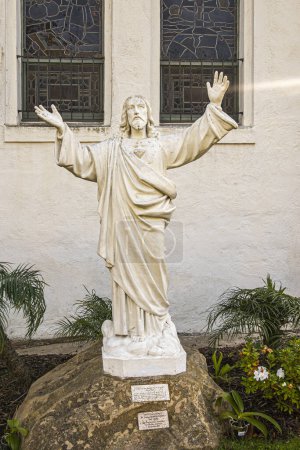 Foto de Santa Bárbara, CA, EE.UU. - 19 de enero de 2024: Primer plano de la estatua blanca del Sagrado Corazón de Jesús en la roca fuera de la iglesia de Nuestra Señora de los Dolores rodeada de follaje verde - Imagen libre de derechos