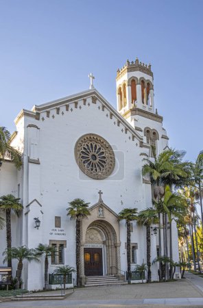 Foto de Santa Barbara, CA, EE.UU. - 19 de enero de 2024: Retrato Entrada principal a la iglesia de Nuestra Señora de los Dolores. Arco esculpido alrededor de madera marrón, engastado en pared blanca con rosas en esquina de la calle - Imagen libre de derechos