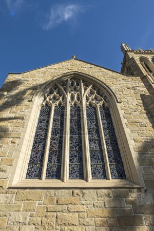 Photo for Santa Barbara, CA, USA - November 30, 2023: Trinity Episcopal Church, closeup of large stained glass window set in sculpted stone frame on State Street. Part of tower. Blue cloudscape - Royalty Free Image