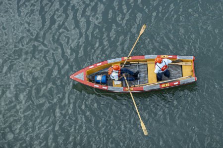 Foto de Canal de Panamá, Panamá - 24 de julio de 2023: 2 chicos con cascos rojos en un pequeño bote de remos consiguiendo cables de barco para enlazar en la máquina en el muelle para tirar de la nave en el bloqueo. Birdseye tiro de primer plano - Imagen libre de derechos