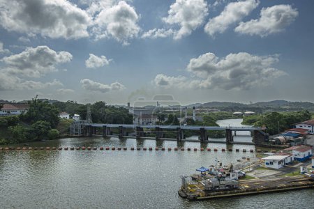 Panama Canal, Panama - July 24, 2023: Thermoelectric plant with tall chimneys under blue cloudscape, down from hydroelectric plant. Most eastern Miraflores locks pier with ship pulling tractor