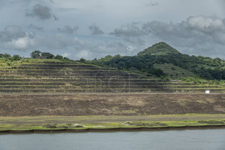 Panama Canal, Panama - July 24, 2023: West shore at Pedro Miguel Locks with terraced farmland and forested hill under blue cloudscape