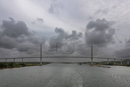 Panama Canal, Panama - July 24, 2023: Atlantic suspension bridge extra wide panorama just out of Canal under gray cloudscape. Colored pipeline floaters in water, Cutter Suction Dredger Quibian 1