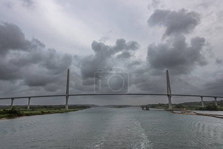 Panama Canal, Panama - July 24, 2023: Atlantic suspension bridge wide panorama just out of Canal under gray cloudscape. Colored pipeline floaters in water, Cutter Suction Dredger Quibian 1