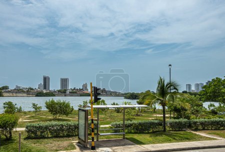 Cartagena, Colombia - July 25, 2023: Public transport stop along Transversal 17 looking over bay water on historic shore walls of old town with few tall buildings under blue cloudscape