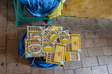 Téléchargez les photos : Cartagena, Colombie - Juillet 25, 2023 : Cigares cubains premium Cohiba en vente hors sac bleu dans la rue de la vieille ville par le vendeur de rue non réglementé. - en image libre de droit
