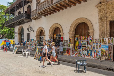 Photo for Cartagena, Colombia - July 25, 2023: In front of Cathedral de Santa Catalina de Alejandra is the Corner of Art and Painters displaying their work for sale. Colorful selection and people, colonial architecture - Royalty Free Image