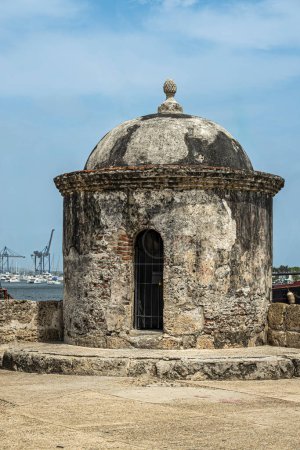 Cartagena, Kolumbien - 25. Juli 2023: Eckwachturm, Bartizan, auf dem Wall Baluarte de San Ignacio und Bastion unter blauer Wolkenlandschaft. Hafen und Teil des Containerterminals am Horizont
