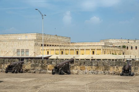 Téléchargez les photos : Cartagena, Colombie - 25 juillet 2023 : Canons sur le rempart et le bastion de Baluarte de San Ignacio. paysage nuageux bleu. Bâtiment du centre de conventions en pierre beige à l'arrière - en image libre de droit