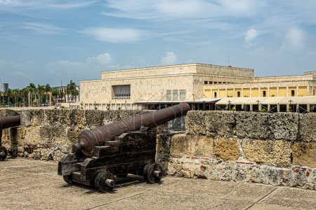 Cartagena, Colombia - 25 de julio de 2023: Cañón en la muralla de Baluarte de San Ignacio y baluarte bajo. paisaje nublado azul. Edificio del Centro de Convenciones de piedra beige en la espalda