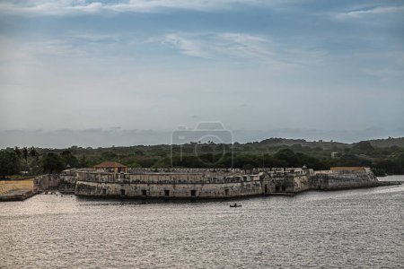 Téléchargez les photos : Carthagène, Colombie - 25 juillet 2023 : Fort, Fuerte de San Fernando de Bocachica remparts au point sud de l'Isla de Tierra Bomba sous un ciel nuageux bleu. Forêt verte à l'arrière - en image libre de droit