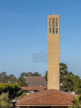 Foto de Santa Barbara, California, Estados Unidos - 17 de marzo de 2024: UCSB, East side of Storke Tower over Karl Geiringer Hall red roof under blue sunny sky. Follaje verde alrededor - Imagen libre de derechos