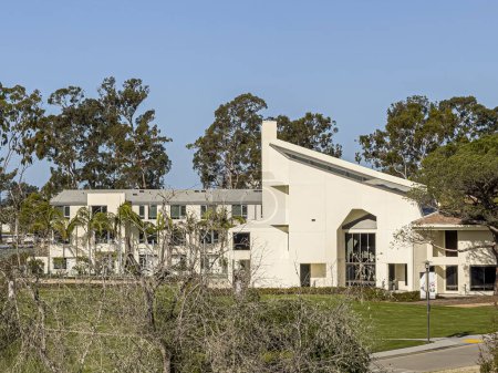 Photo for Santa Barbara, California, USA - March 17, 2024: UCSB, The Club and Guest House east beige facade under blue sunny sky with green foliage behind - Royalty Free Image