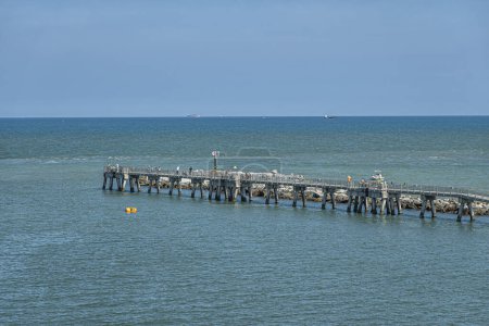 Port Canaveral, Florida, USA - July 30, 2023: Fisherman Pier with boardwalk stretches into blue water Atlantic Ocean. Pedestrians and active fishers present. Blue sky. Ship on horizon