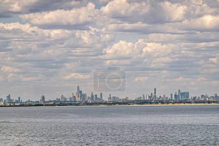 New York, NY, USA - 1. August 2023: Stadtsilhouette vor Ozean unter blauer Wolkenlandschaft. Ein World Trade Center ist das höchste. Grünes Dach ist Bundeshalle. Sandstrand von Bel Harbor