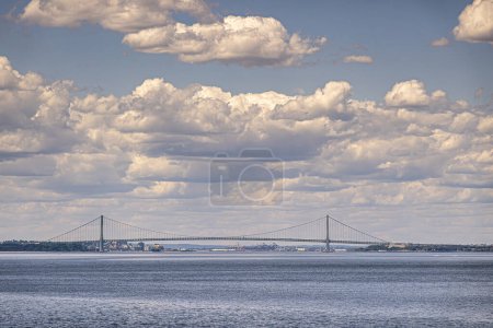 Nueva York, NY, Estados Unidos - 1 de agosto de 2023: Verrazzano-Narrows puente colgante visto desde el sur bajo un paisaje nublado azul con agua azul del océano por delante. Fortalezas Wadsworth y Hamilton verdes