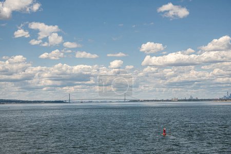 New York, NY, USA - 1. August 2023: Verrazzano-Narrows Hängebrücke südlich des Meeres unter blauer Wolkenlandschaft mit blauem Meerwasser davor. Forts Wadsworth und Hamilton Grüns