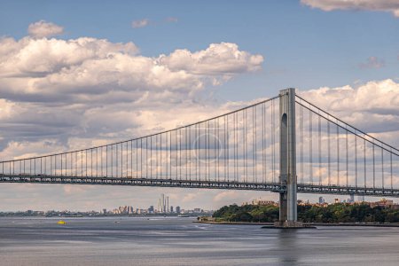 Nueva York, NY, EE.UU. - 1 de agosto de 2023: Rascacielos de Jersey City bajo el puente Verrazzano-Narrows. Nubosidad azul arriba. Green Hamilton Fort Park en la costa. Aguas de la bahía superior con buques
