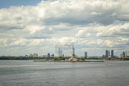 New York, NY, USA - August 1, 2023: Statue of Liberty on its island in wide landscape showing New Jersey coastline under blue cloudscape