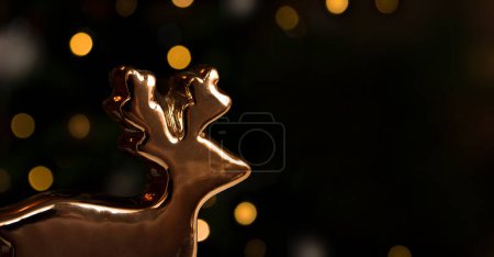 Photo for Golden deer figurine on a blurry dark background with bokeh. Celebrating christmas and New Year. Winter holiday theme. Space for text . Banner - Royalty Free Image