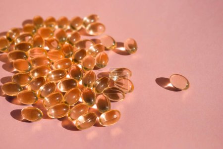 Photo for Golden capsules of fish oil  close up are scattered on a pink or pale pink background with deep shadows. Medical healthcare. Vitamin tablets. Copy space. Space for text - Royalty Free Image