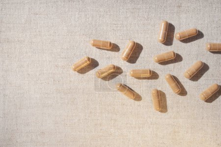 Photo for Brown capsules are scattered close up on a beige tablecloth table background. Dietary supplement capsules. Copy space. Space for text - Royalty Free Image