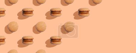 Beige color macaroons cookies on a peach fuzz background with shadows. Space for text. Minimal food dessert concept. Copy space. Banner