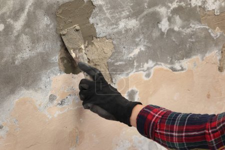 Photo for Worker fixing cracks and damages on wall, hand in glove spreading plaster using trowel - Royalty Free Image