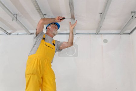 Foto de Trabajador colocando perfil de aluminio para techo de yeso y aislamiento usando destornillador - Imagen libre de derechos