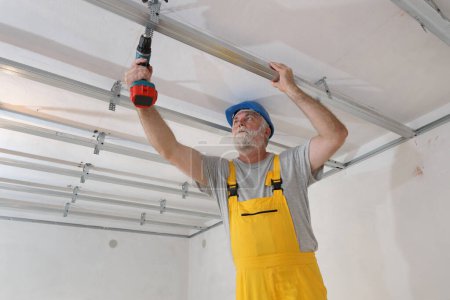 Foto de Trabajador que coloca el perfil de aluminio para el techo de yeso y el aislamiento usando la herramienta eléctrica del destornillador - Imagen libre de derechos