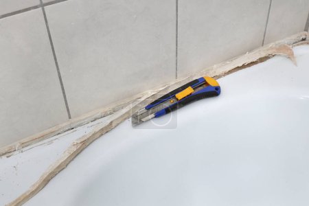 Foto de Eliminación de silicona sucia vieja del tubo de baño en un baño, corte de pegamento de silicona con cortador, renovación del baño - Imagen libre de derechos