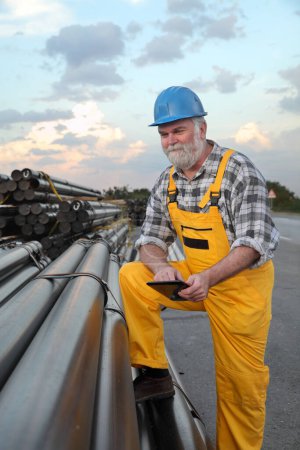 Foto de Trabajador sonriente con tableta en las manos y montón de tubos aislados para gas natural - Imagen libre de derechos