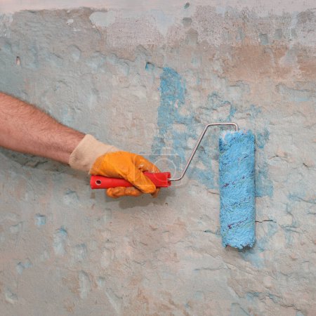 Foto de Mano del trabajador que usa rodillo de pintura para aplicar líquido de imprimación adhesivo para pegar baldosas - Imagen libre de derechos