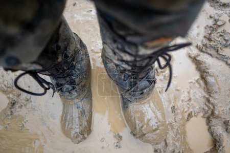 Foto de Close-up for a man's legs in military camouflage with a trekking wellington shoes dirty in mud. - Imagen libre de derechos
