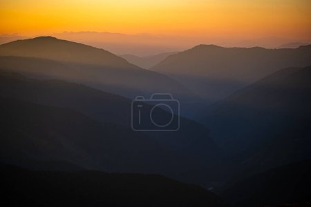 Siluetas oscuras de montañas al amanecer con un cielo anaranjado. Fondo oscuro con un espacio de copia. Las montañas Parang, Rumania.