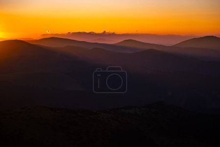 Téléchargez les photos : Silhouettes sombres de montagnes au lever du soleil avec un ciel orange. Fond sombre avec un espace de copie. Les monts Parang, Roumanie. - en image libre de droit