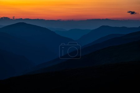 Téléchargez les photos : Silhouettes sombres de montagnes au lever du soleil avec un ciel orange. Fond sombre avec un espace de copie. Les monts Parang, Roumanie. - en image libre de droit