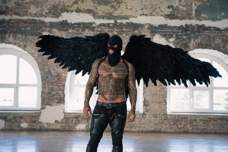 Foto de Male angel with black wings. Black angel in a mask. Muscular shirtless man with whip in a mask.Brutal handsome man with tattooed body. Muscular athletic sexy male with naked torso. hot man - Imagen libre de derechos