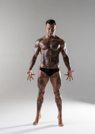 Foto de Young handsome bodybuilder posing,  athlete shows bodybuilding posing. hot tattoed man with beautiful body shows his muscles in the studio - Imagen libre de derechos